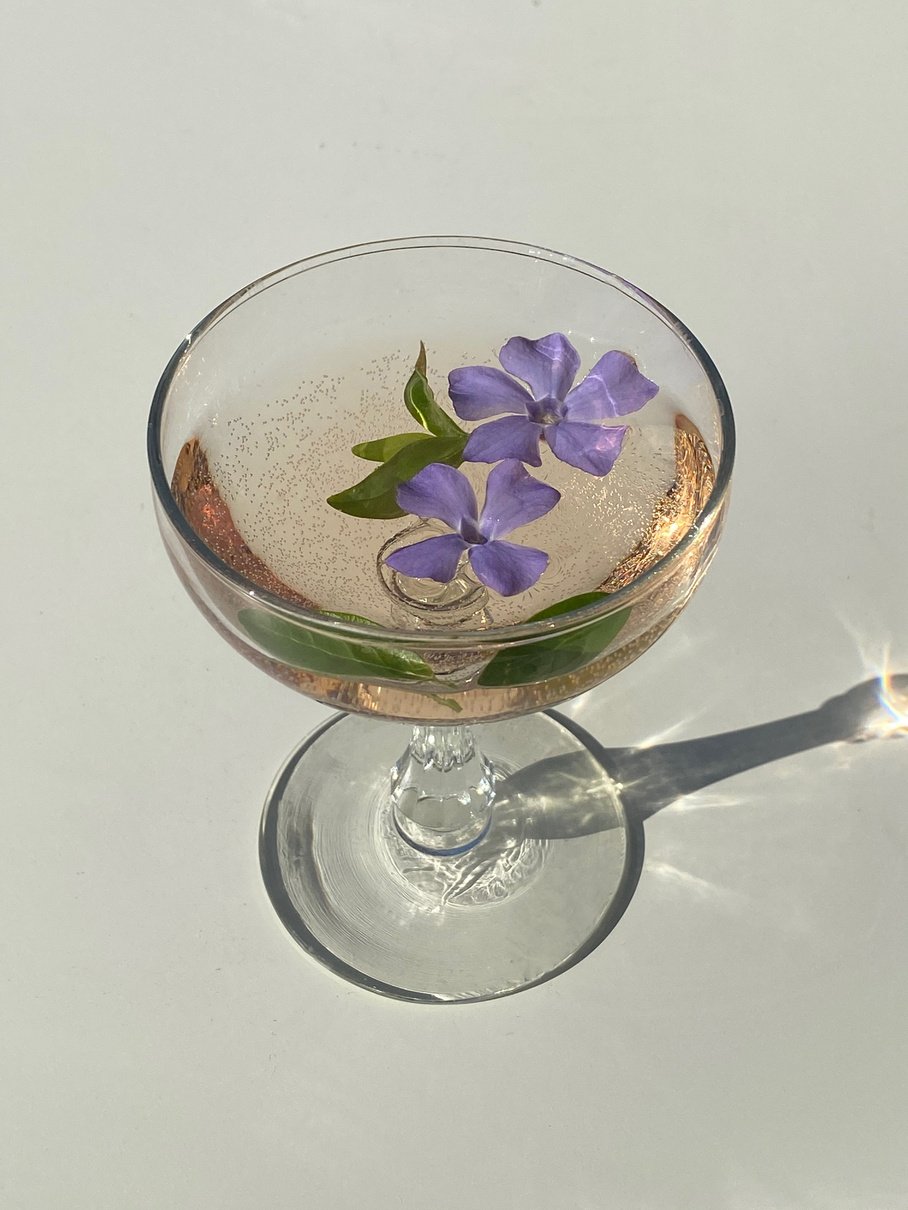 Glass with cocktail with flowing flowers of Vinca minor